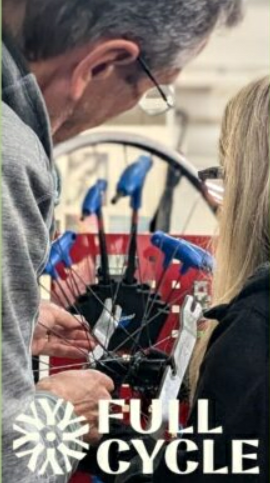 Close up of two people working on a bicycle wheel