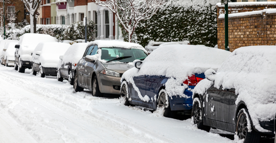 A photo of a residential street with cars and road covered in deep snow